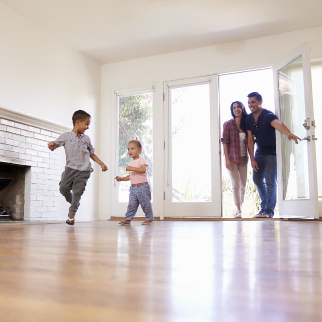 A young family of four excitedly moving into a brand new house with hardwood floors and white walls