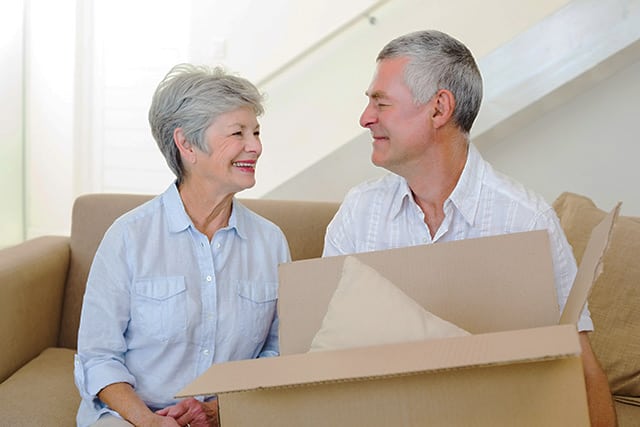 Older couple smiling at each other, holding a cardboard box in preparation for a move