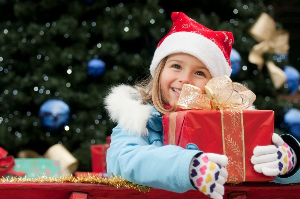 Young girl wearing a Santa cap smiling and holding a red package with a bow