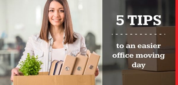 A woman in a denim shirt holding a moving box with a houseplant and books preparing to move her office